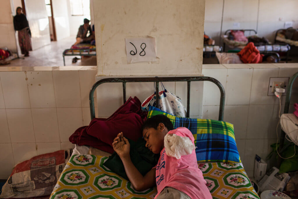 Mohammad F., 15, receives treatment at Cox's Bazar General Hospital. The Myanmar Army opened fire on him as he fled his village in September 2017, leading to the loss of his left arm. His uncle covered the wound with medicinal leaves while they hid in the jungle for five weeks before arriving in Bangladesh. He is with his brother, 10, and sister, 7; their parents' whereabouts are unknown.  Patrick Brown © Panos/ UNICEF 2018